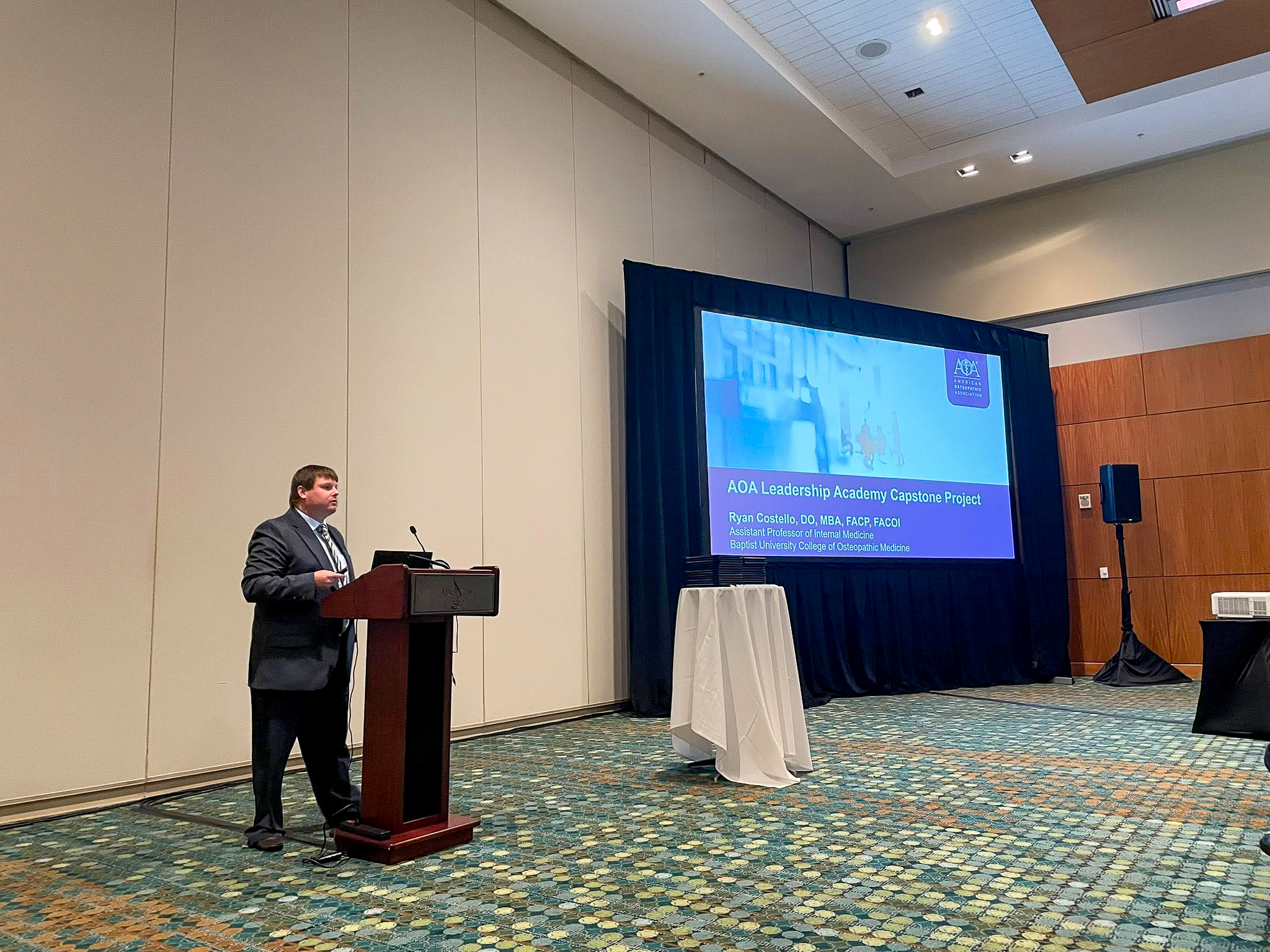 Dr. Ryan Costello presents his AOA Leadership Academy Capstone Project at OMED 2025 in a conference room setting.