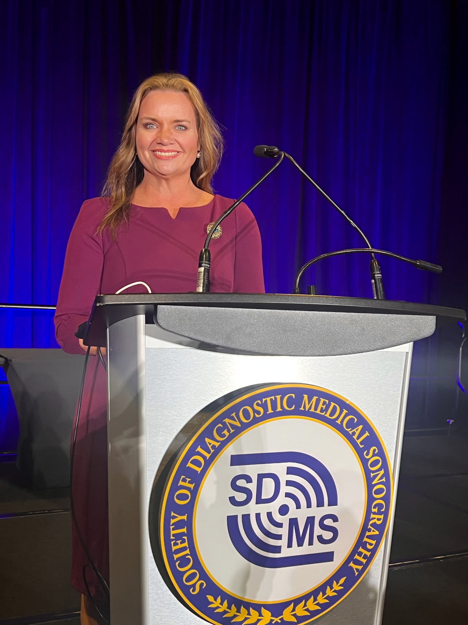 Mitzi Roberts standing behind a podium smiling at the camera