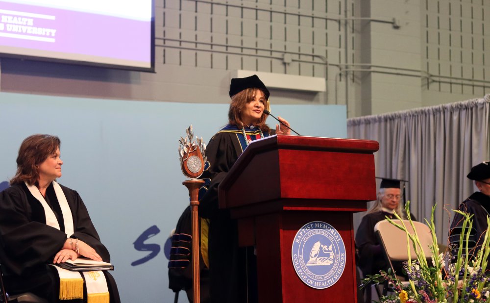 Speaker in academic regalia stands behind a wooden podium 