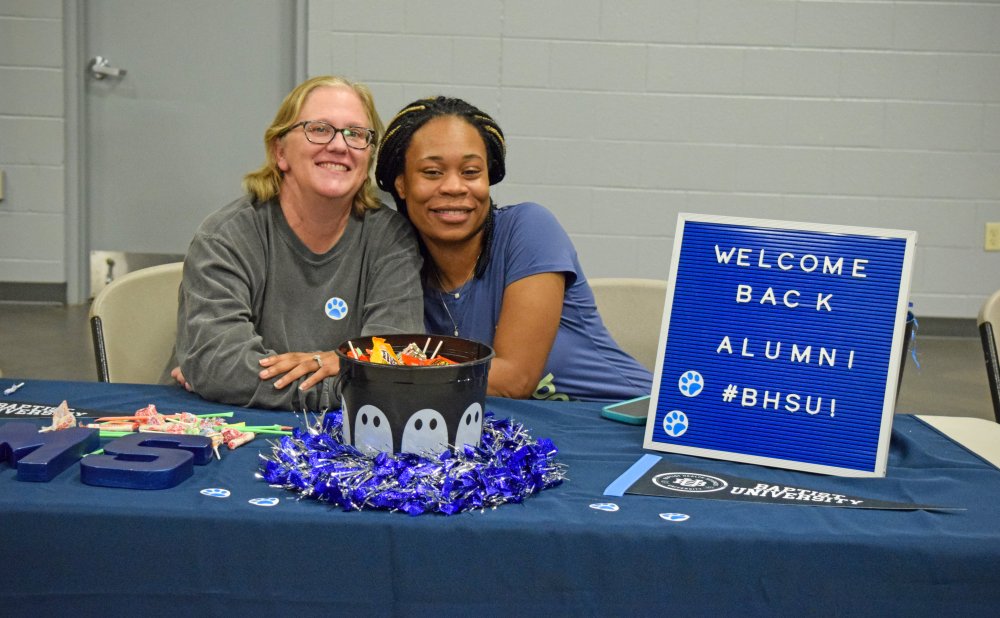 Alumni in blue shirt hugging program chair from sonography program with a welcome back alumni sign 