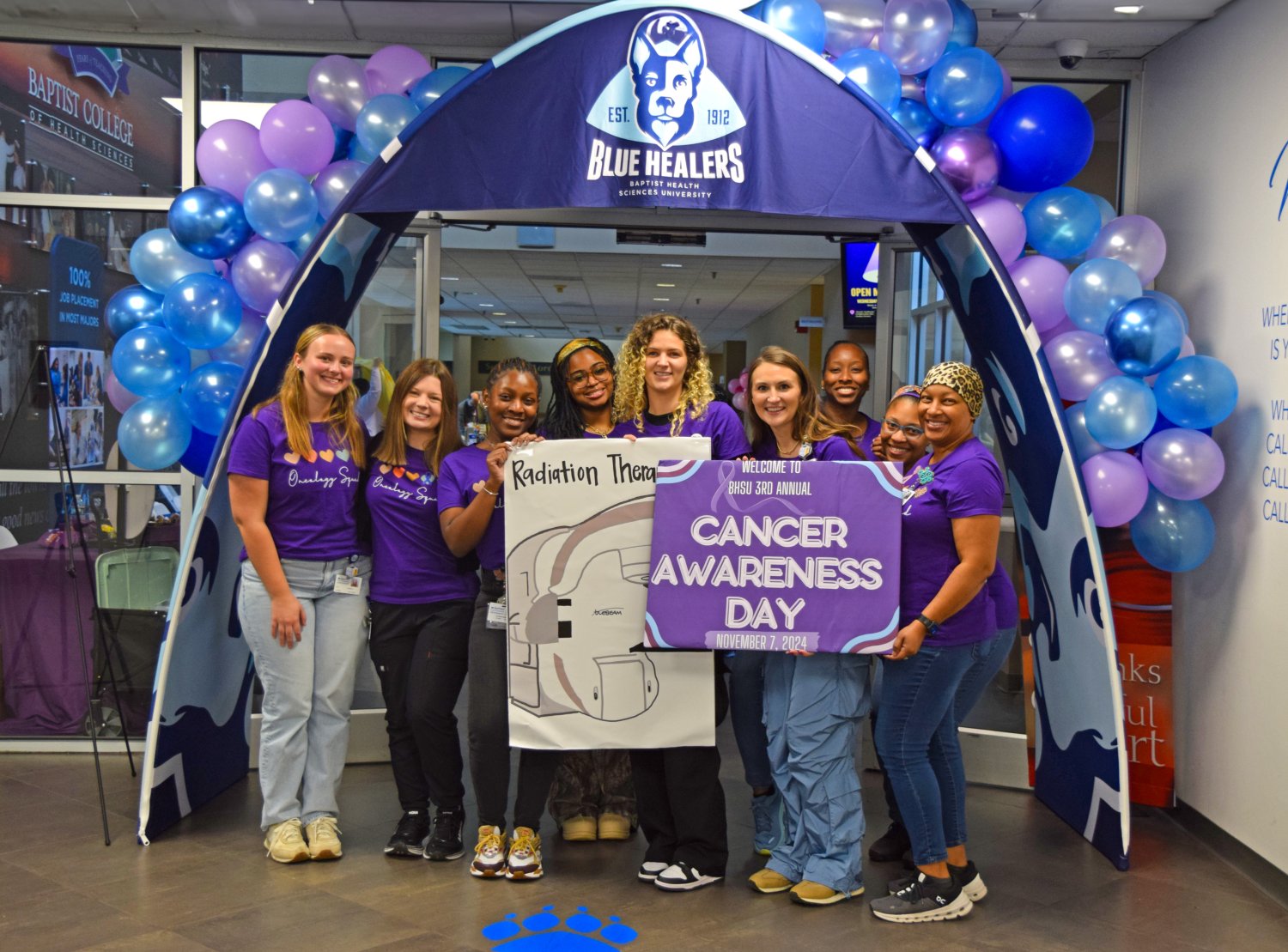 Radiation Therapy students and professor standing in the front of the entryway with a sign that reads cancer awareness day