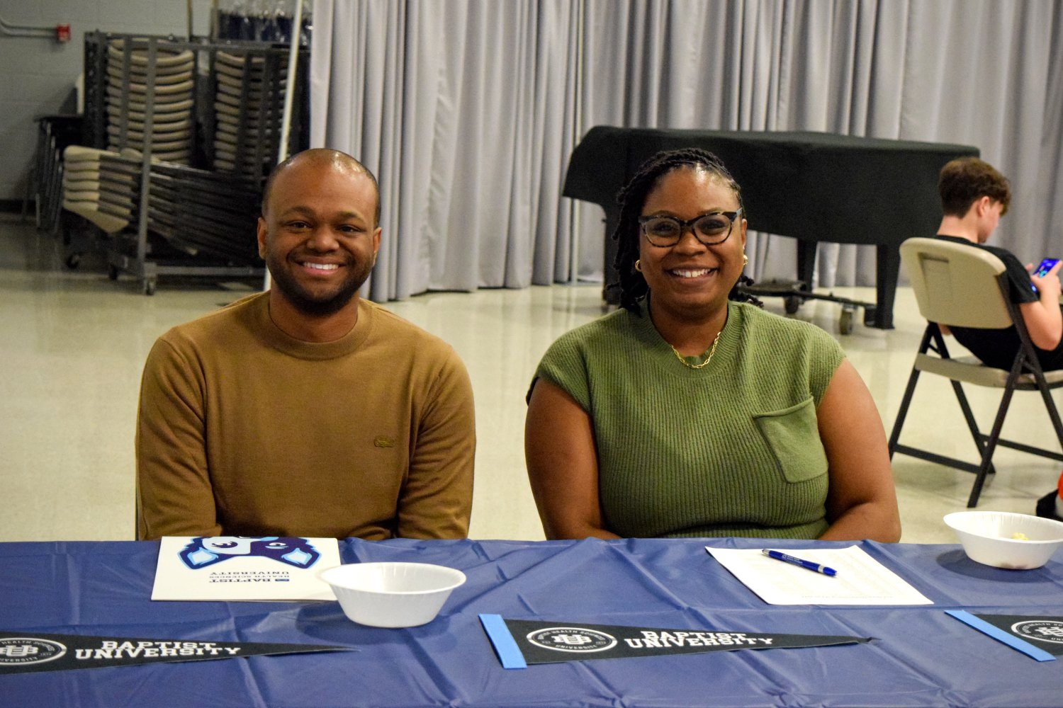 2 Alumni smiling at the welcome booth for the homecoming event 