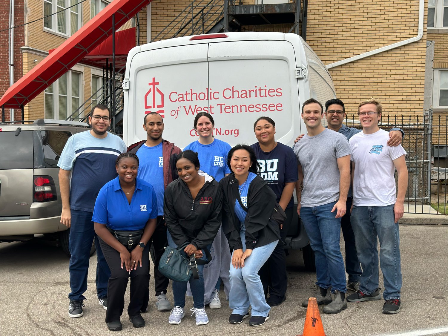 A group of BUCOM Students in front of a truck that states Catholic Charities of West TN taking a photo