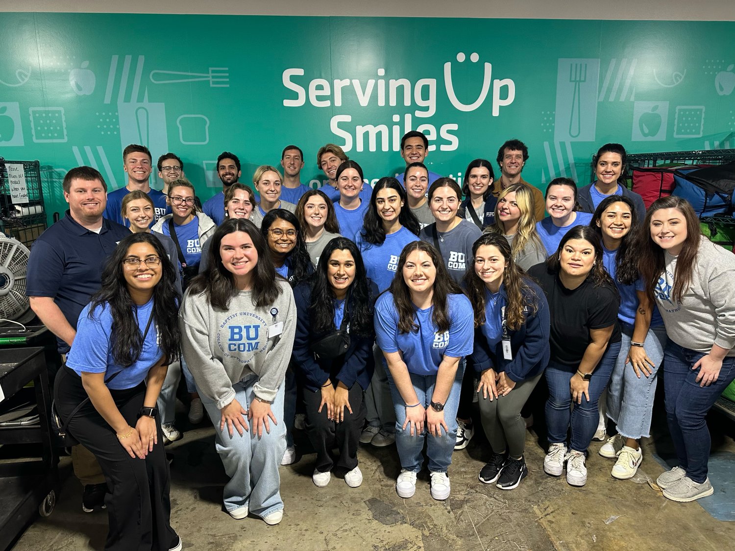 A crowd of BUCOM students gathered in front of the serving up smiles sign taking a photo